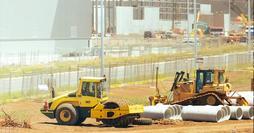 Construction site with heavy machinery and concrete pipes being prepared for installation