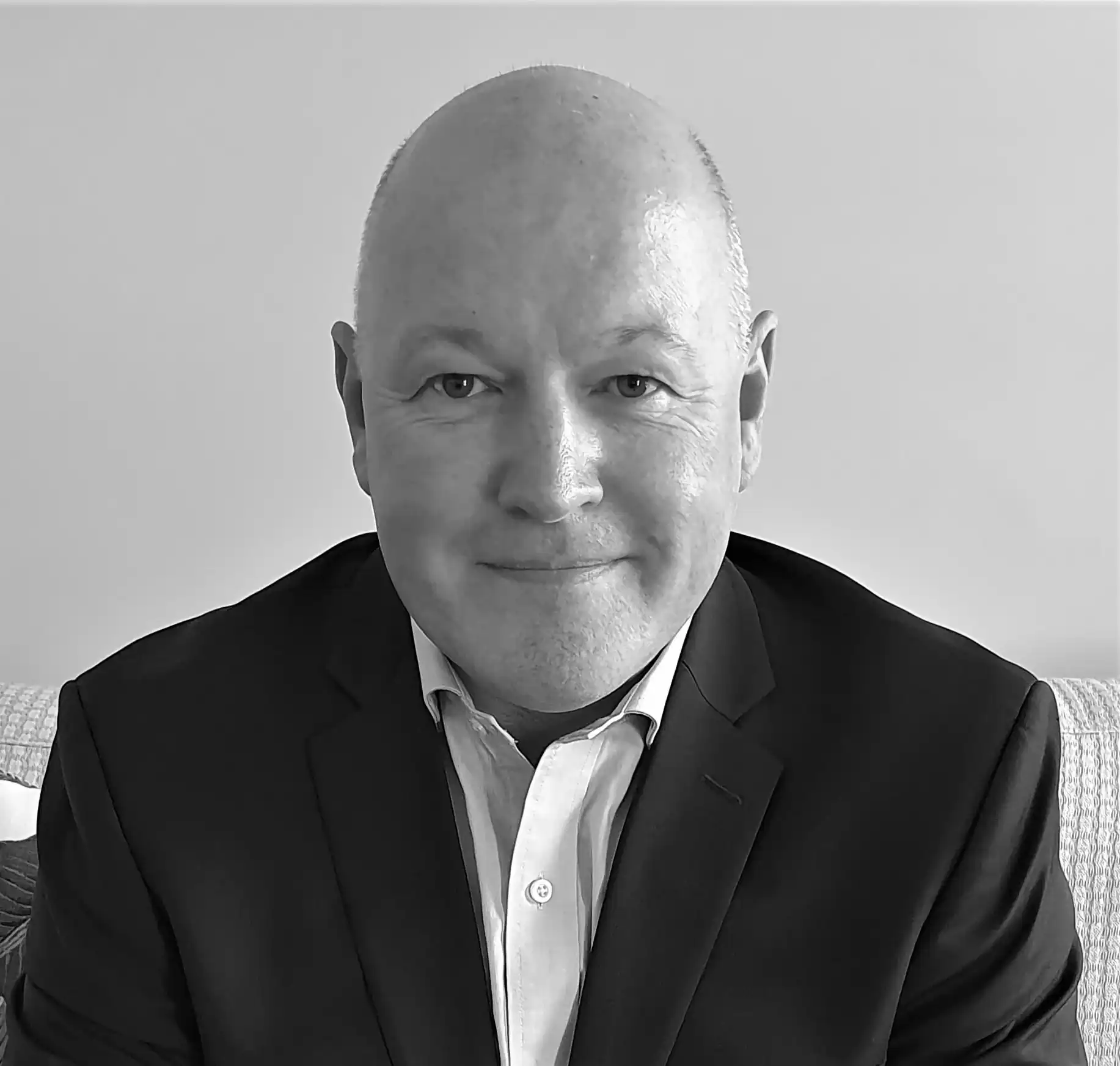 Portrait of a senior business leader wearing a suit, seated indoors against a neutral background.