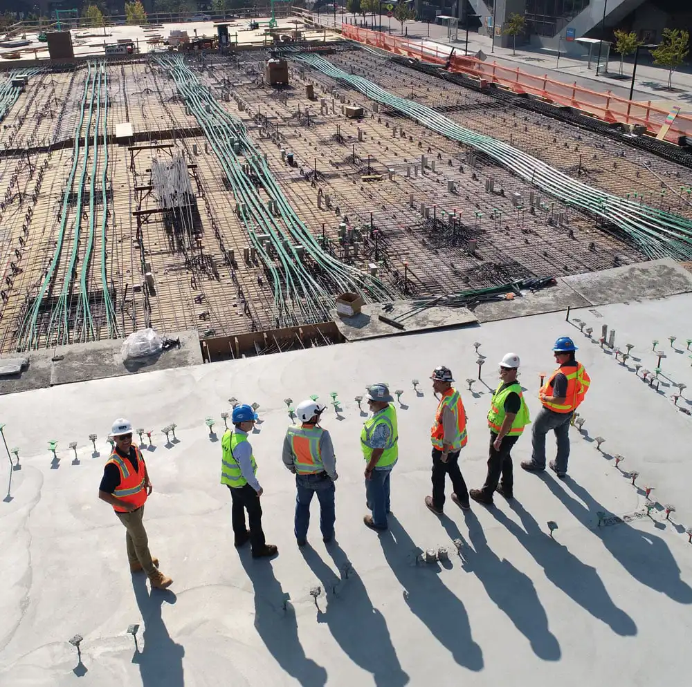 Group of construction professionals standing on a concrete slab during a site inspection overlooking infrastructure works.