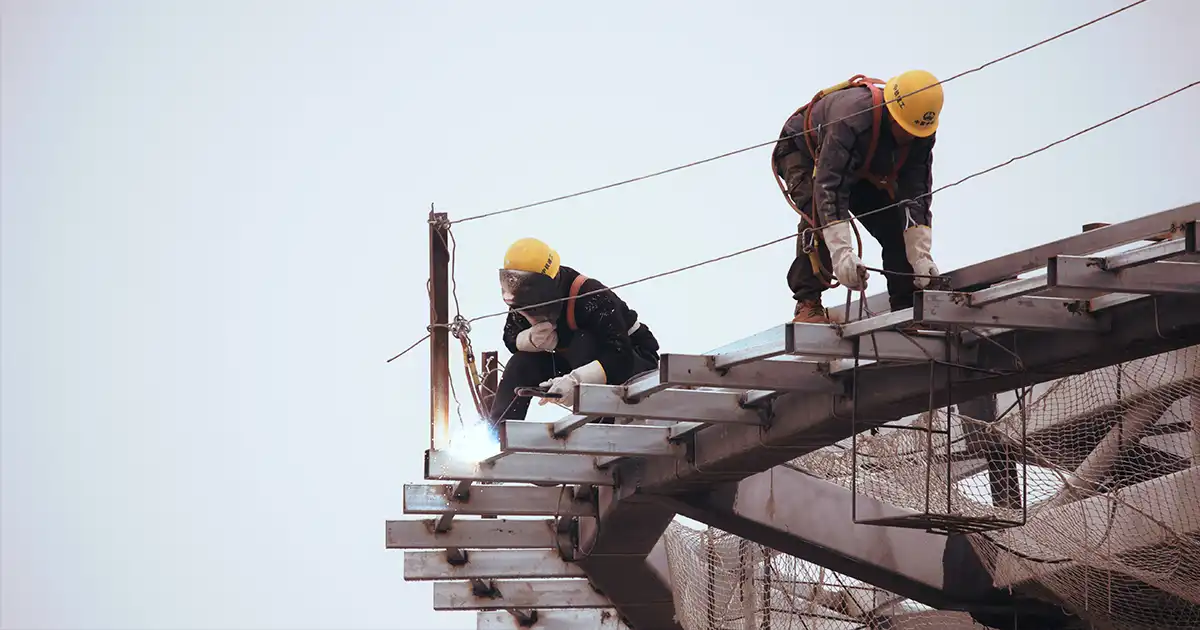 Workers in safety gear welding structural steel on a construction site, illustrating on-site operations.